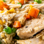 A plate of crockpot chicken and rice with carrots and peas.