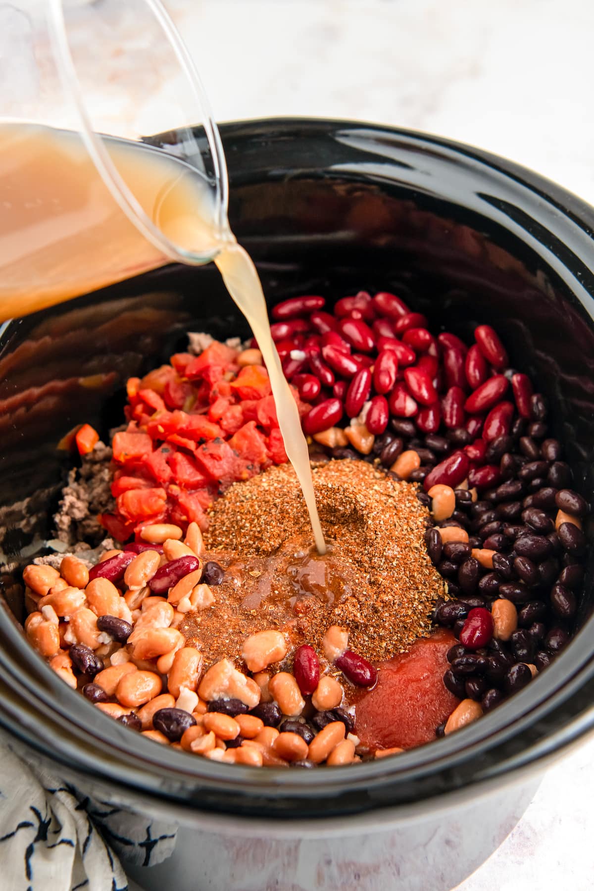 adding stock to a crockpot with beans, beef, and seasoning