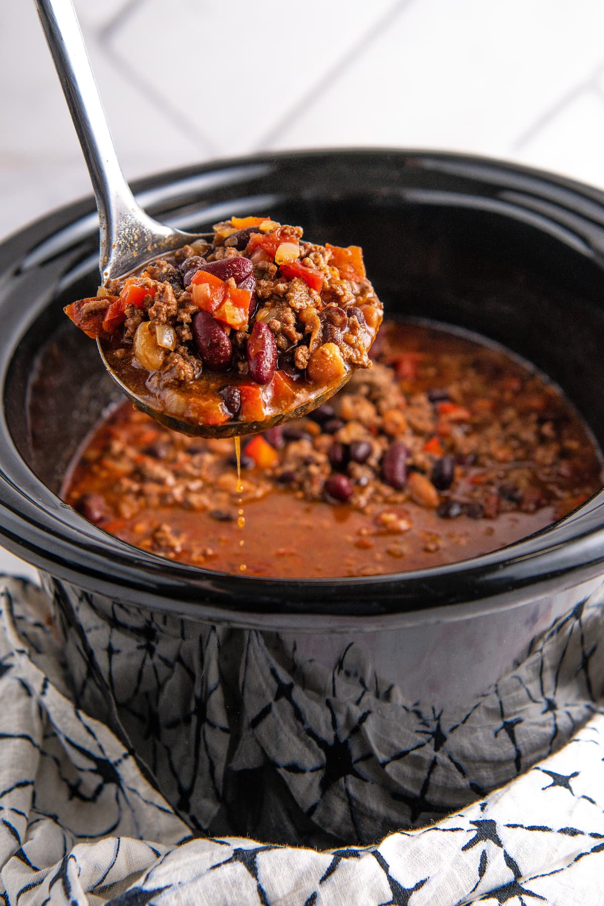 a ladle taking a scoop of chili out of a crockpot