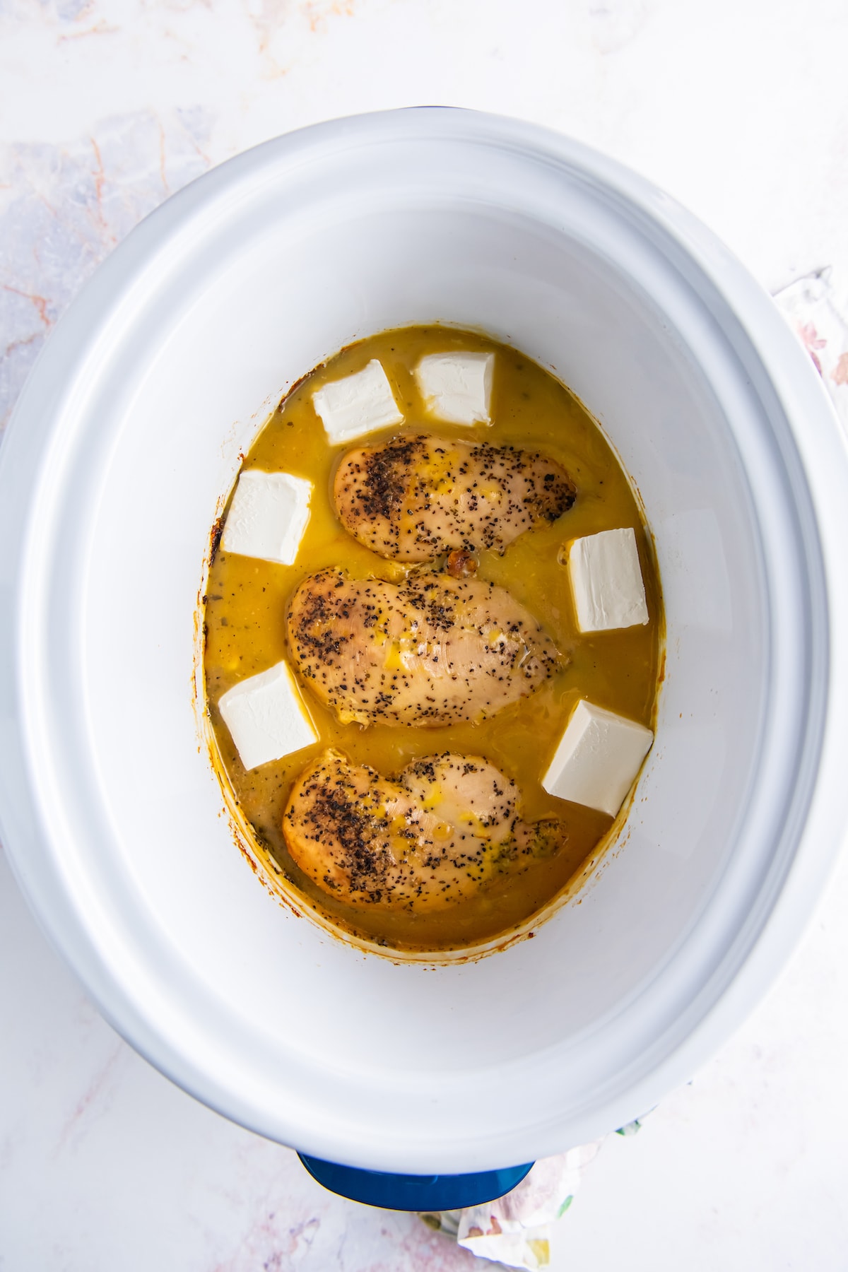 three chicken breasts with broth and cream cheese in a crockpot