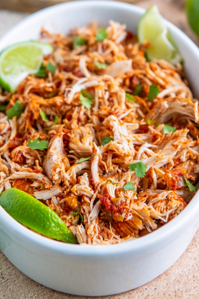 a casserole dish with shredded chicken tossed in salsa and fresh herbs