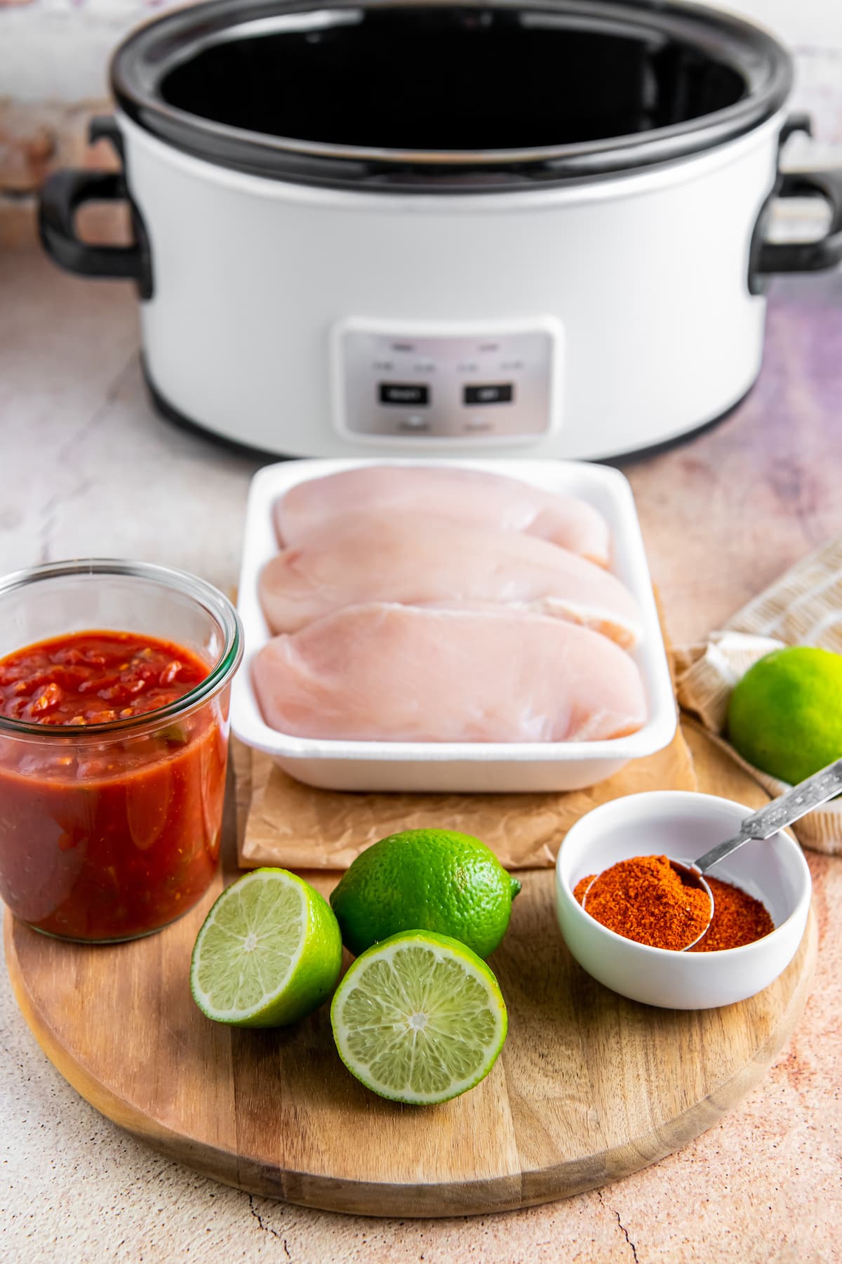 an assortment of ingredients including chicken, limes, seasoning, and salsa on a cutting board