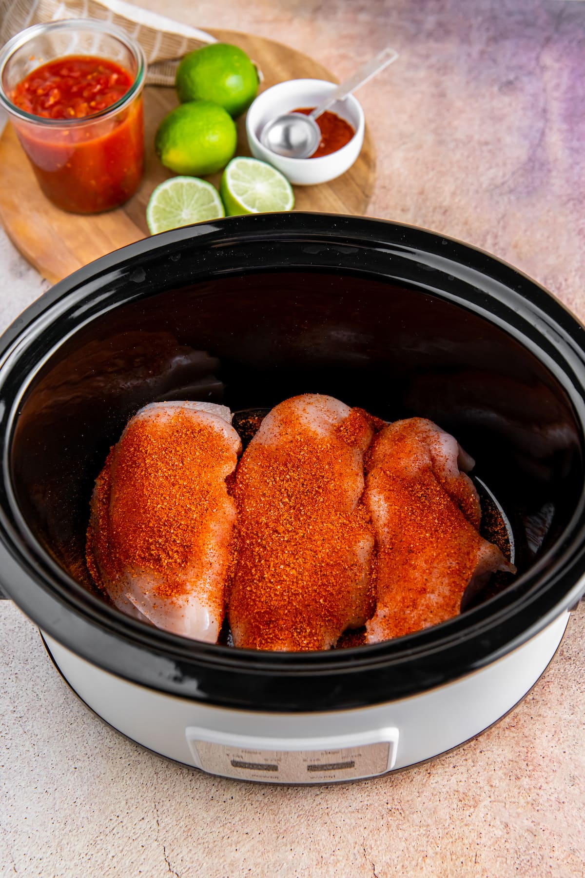 three raw chicken breasts in a crockpot with seasoning on them