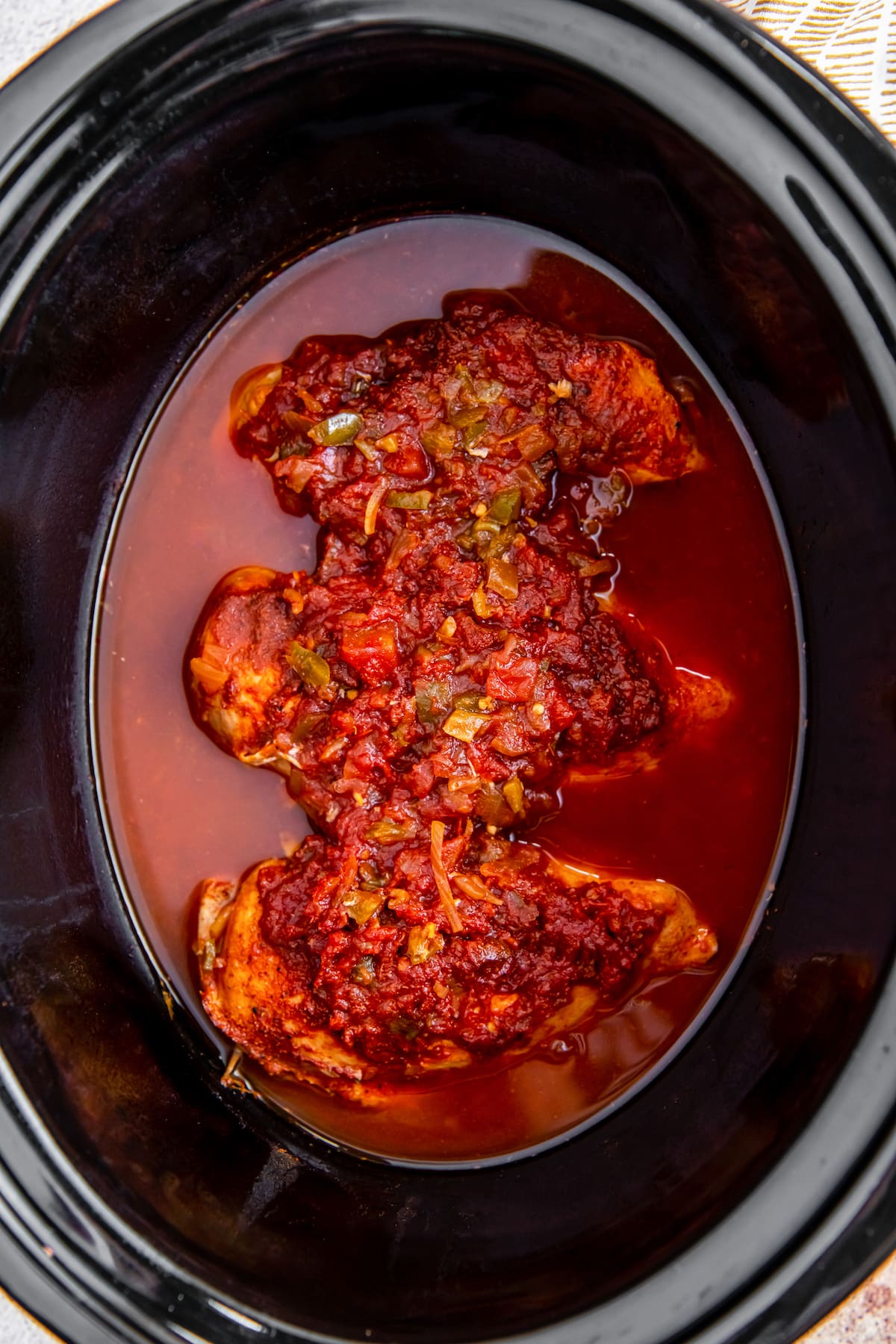 three cooked chicken breasts in a crockpot with salsa