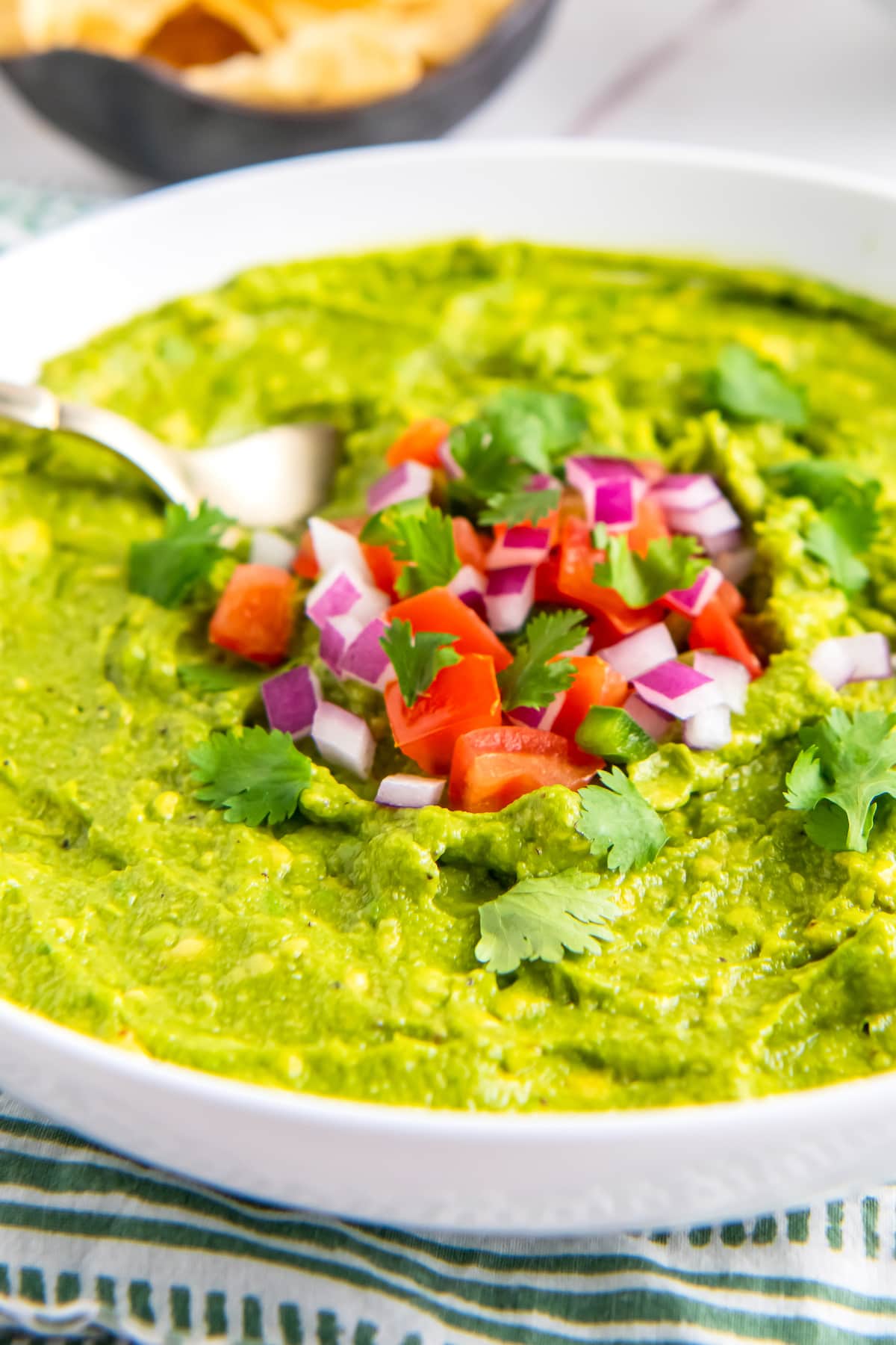 a bowl of guacamole with tomato, red onion, and jalapeno garnish