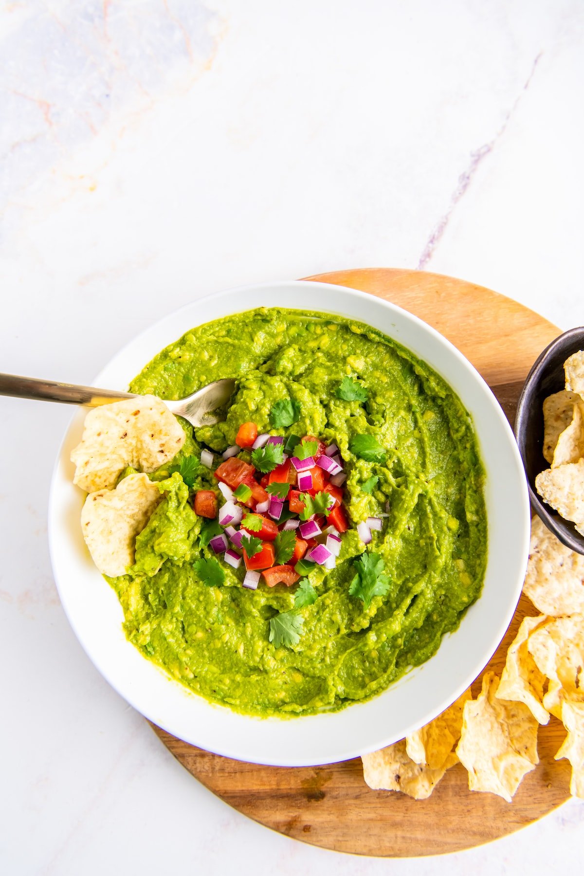 a bowl of avocado dip on a round wooden cuting board with tortillas on the side