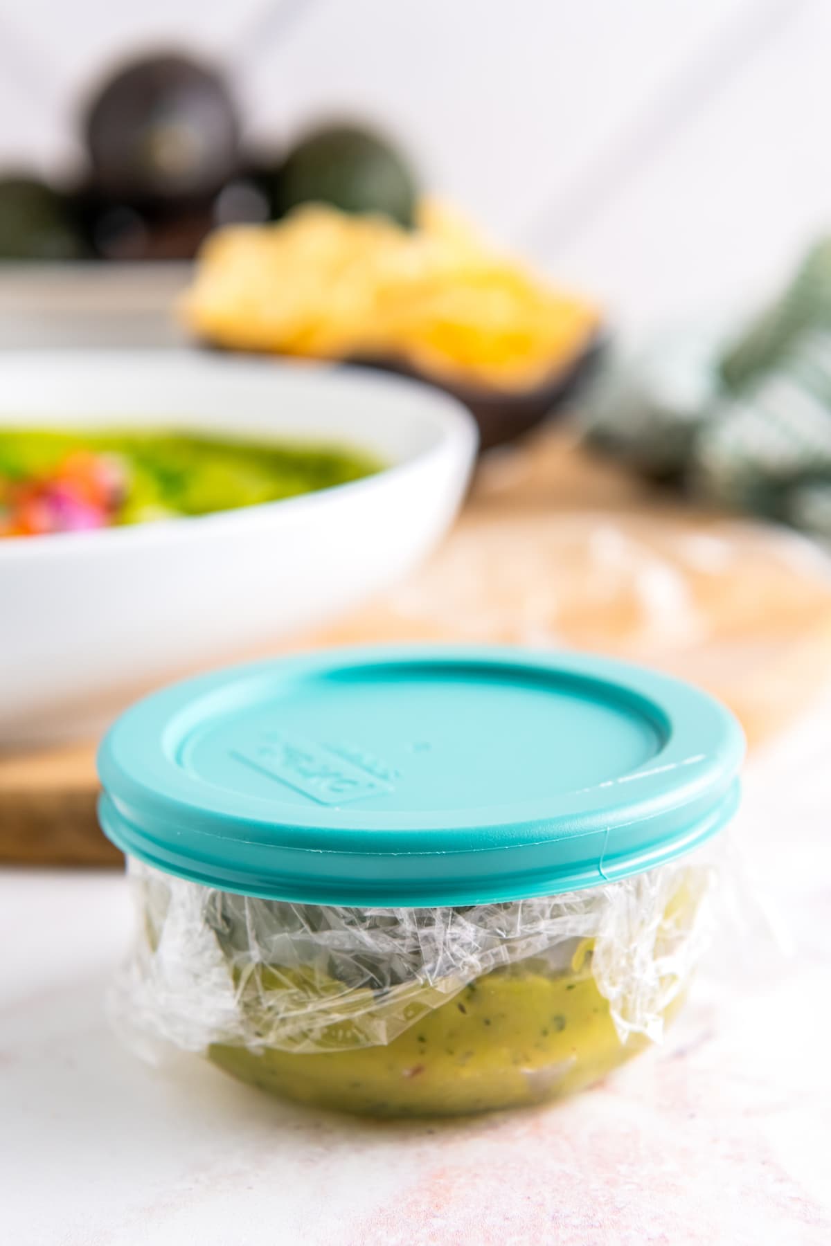 a small storage container with plastic wrap and guacamole on the inside