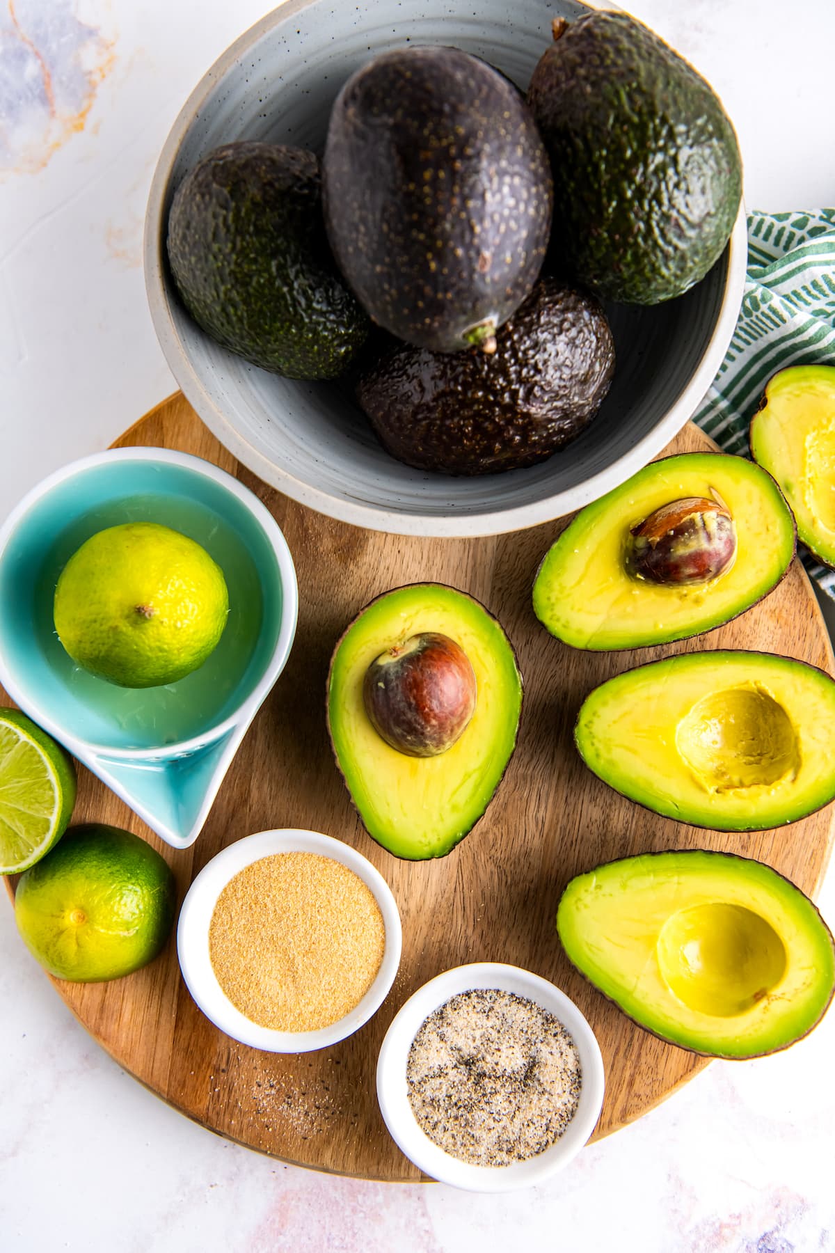 cut up avocados, seasonings, and limes on a round cutting board