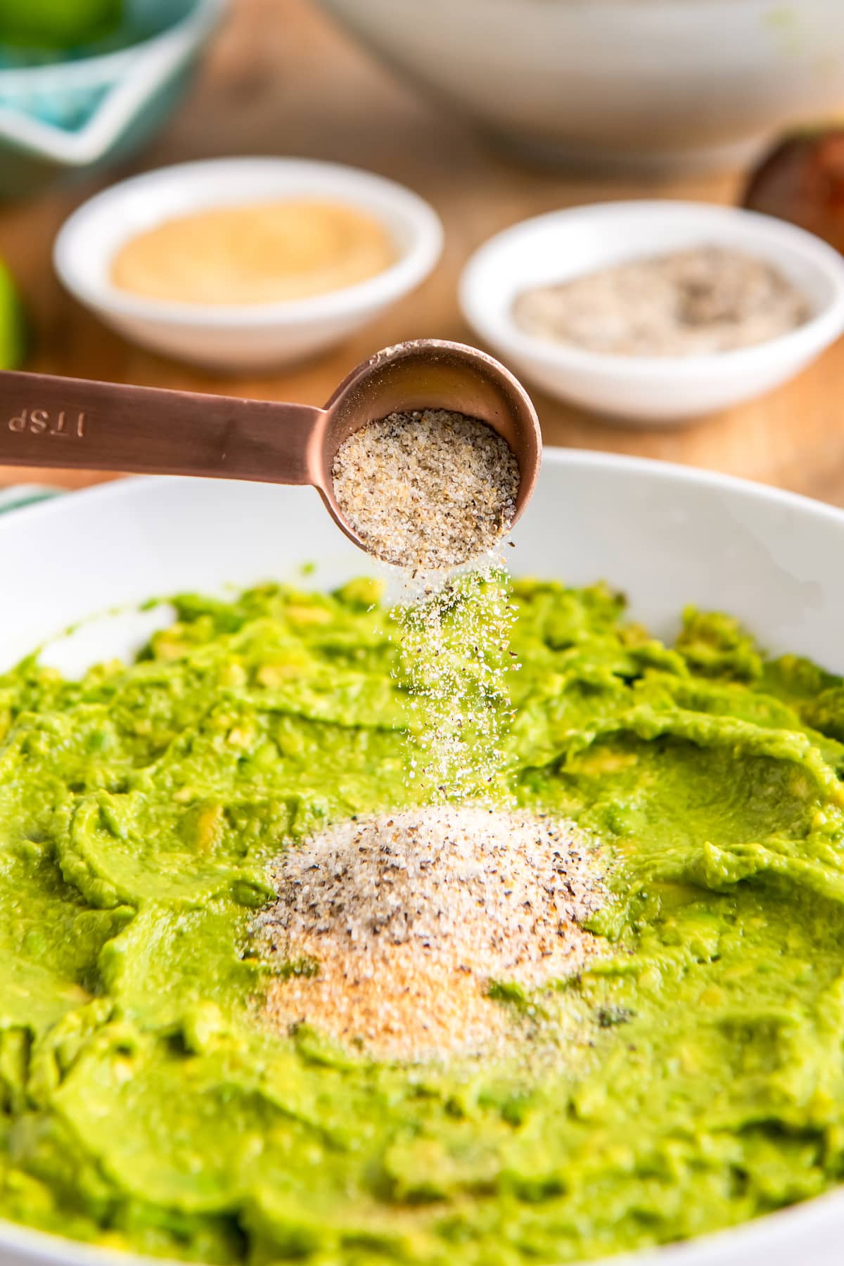 seasoning smashed avocados in a white bowl