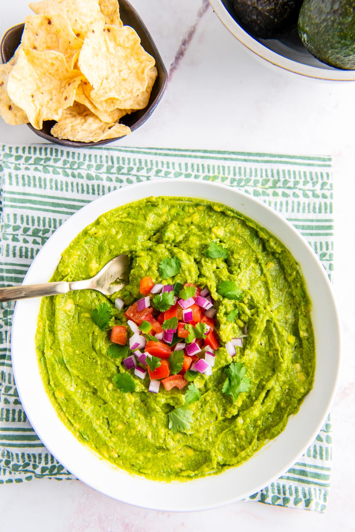 a bowl of guacamole with tomato, red onion, and jalapeno garnish