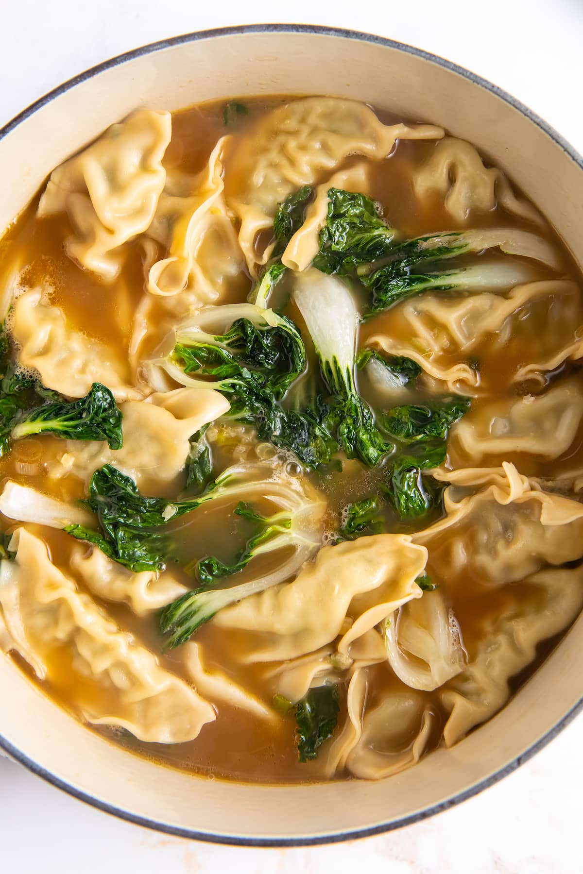 cooked dumplings in broth with greens in a large pot making potsticker soup