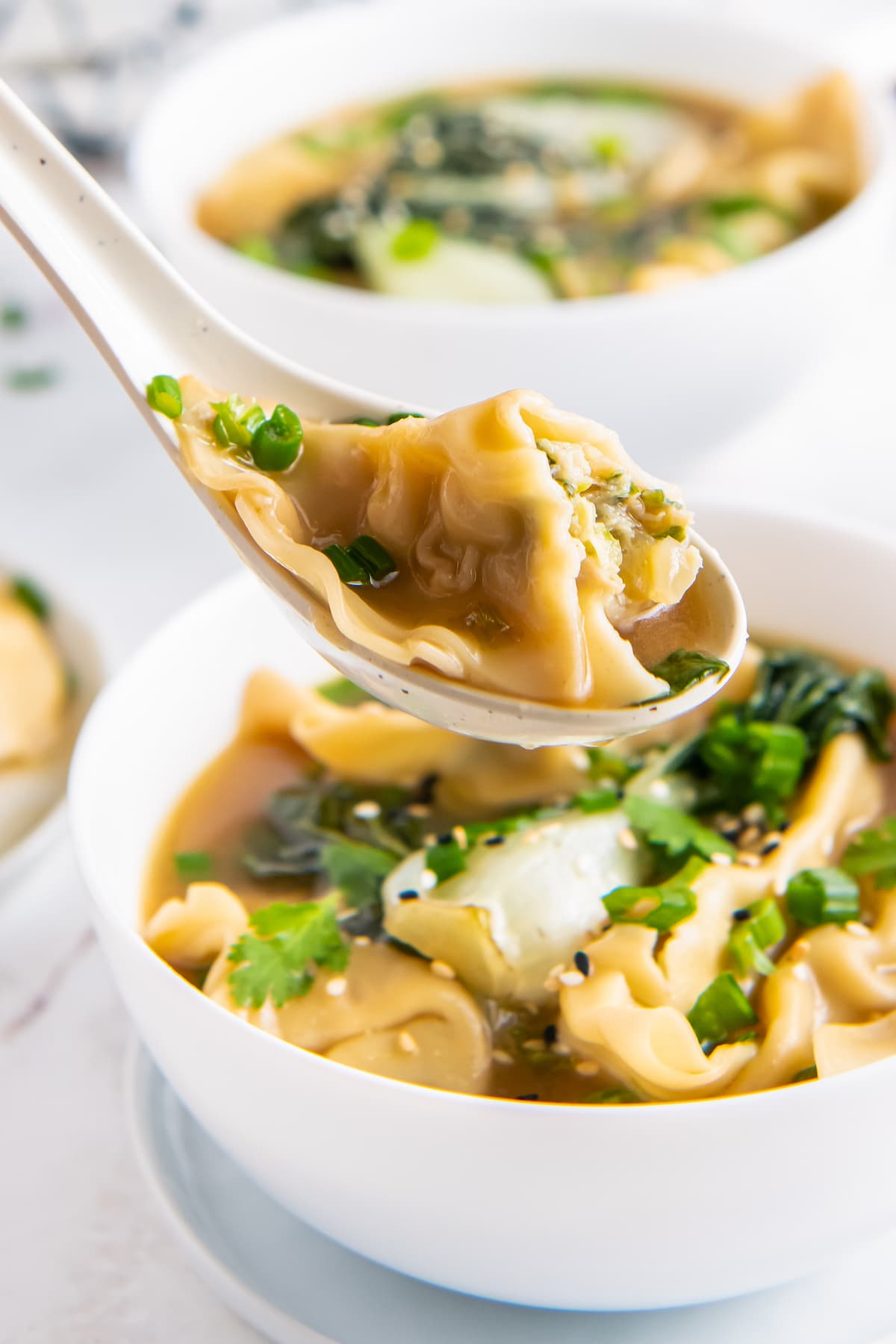 potsticker soup with herbs and bok choy in a white bowl with a spoon taking a bite