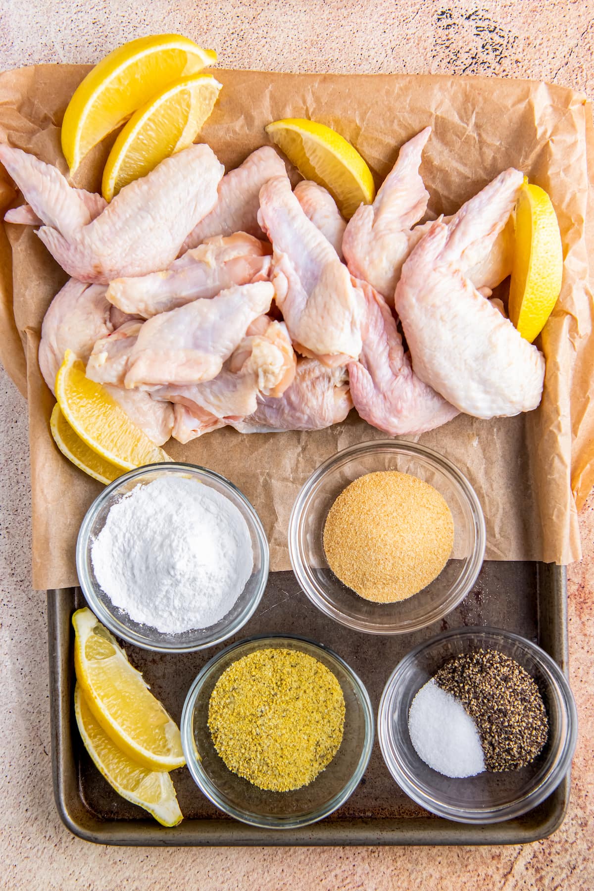 ingredients to make lemon pepper chicken wings like raw wings and seasonings on a sheet tray