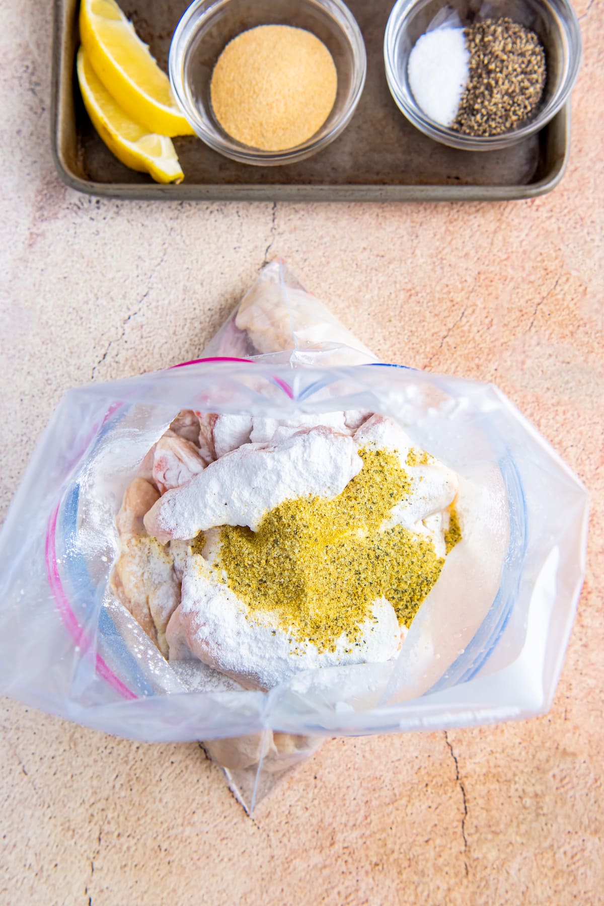 top view of a plastic bag with chicken wings and seasonings dumped on top of them