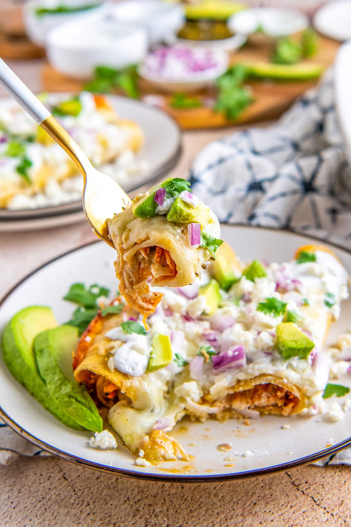 a fork with a bite of enchilada on it over a plate