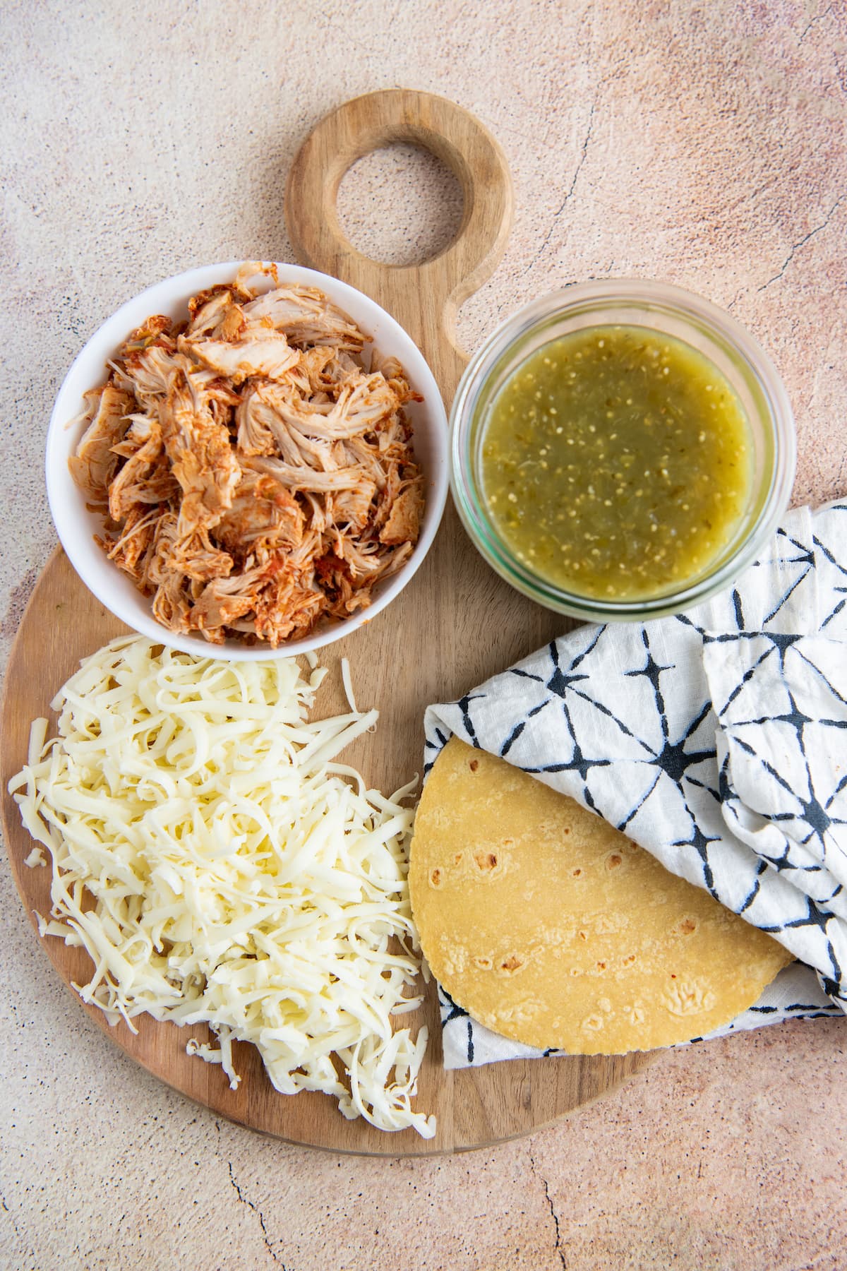 a wooden cutting board with shredded chicken, sala verde, cheese, and tortillas