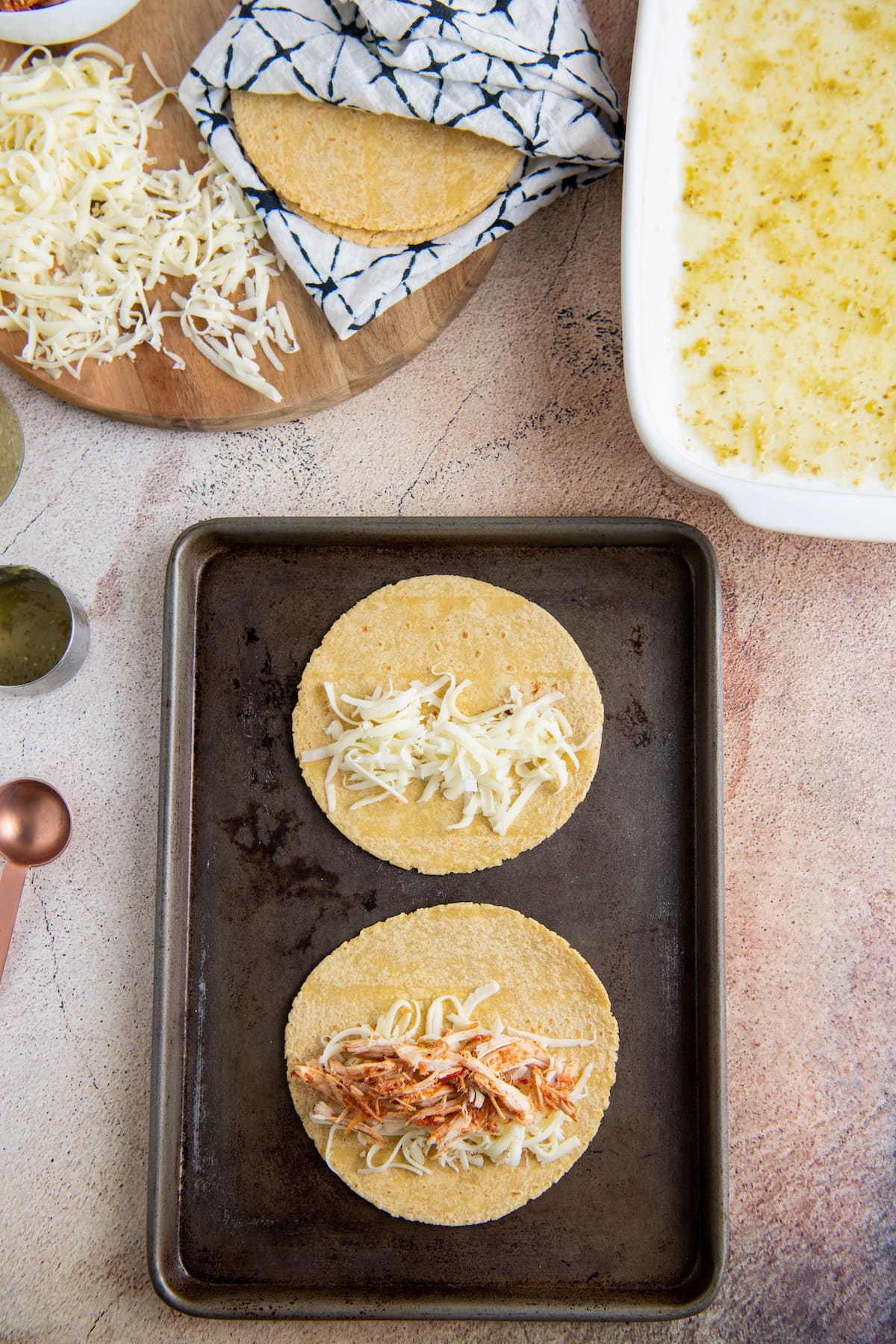 a sheet tray with two tortillas with cheese and shredded chicken being put into them