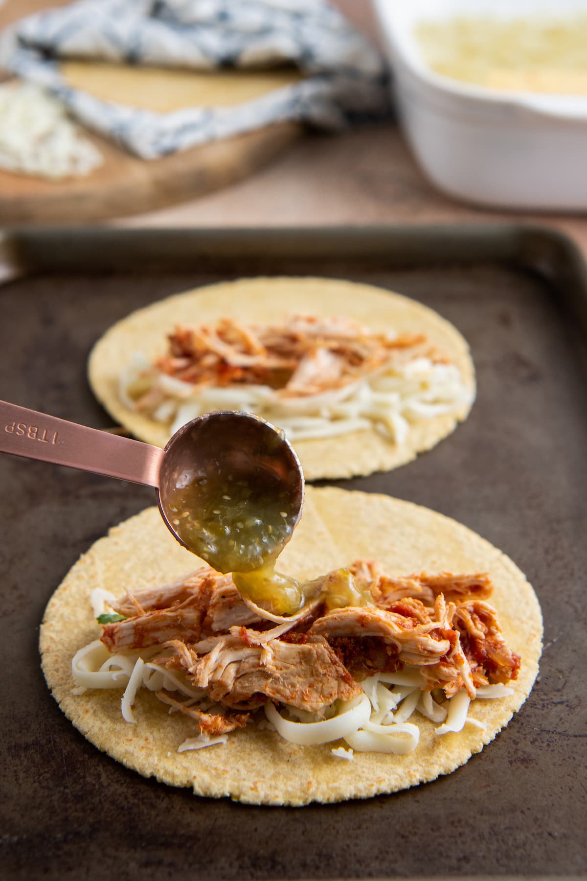 adding salsa verde to a tortilla on a sheet tray with chicken and cheese