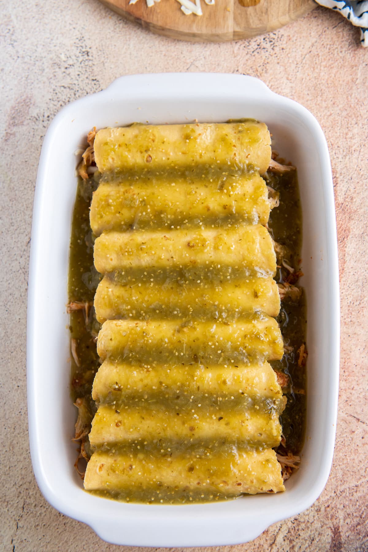 rolled enchiladas in a casserole dish with salsa verde poured on top