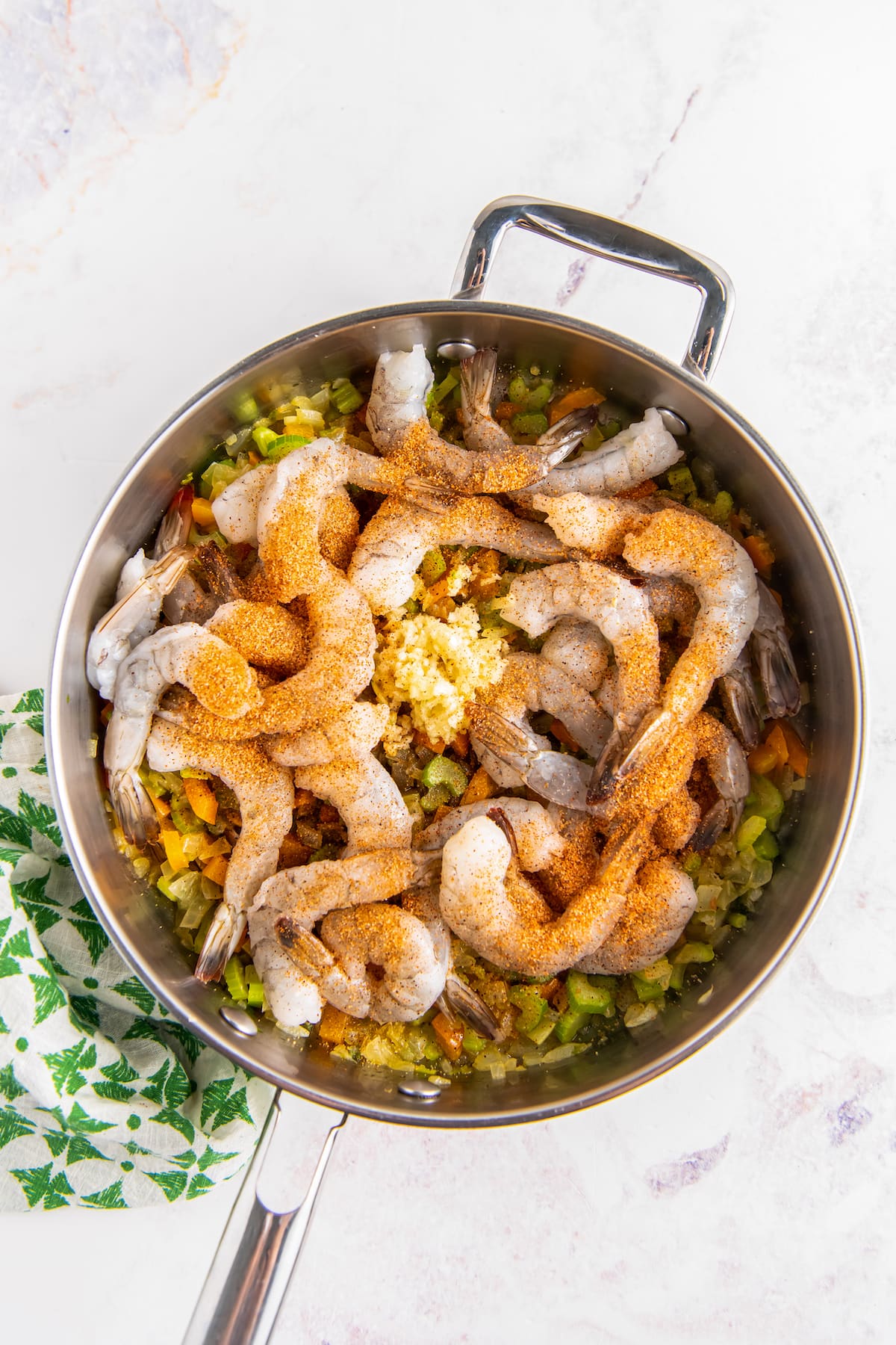 adding raw shirmp to a pan with cooked diced vegetables