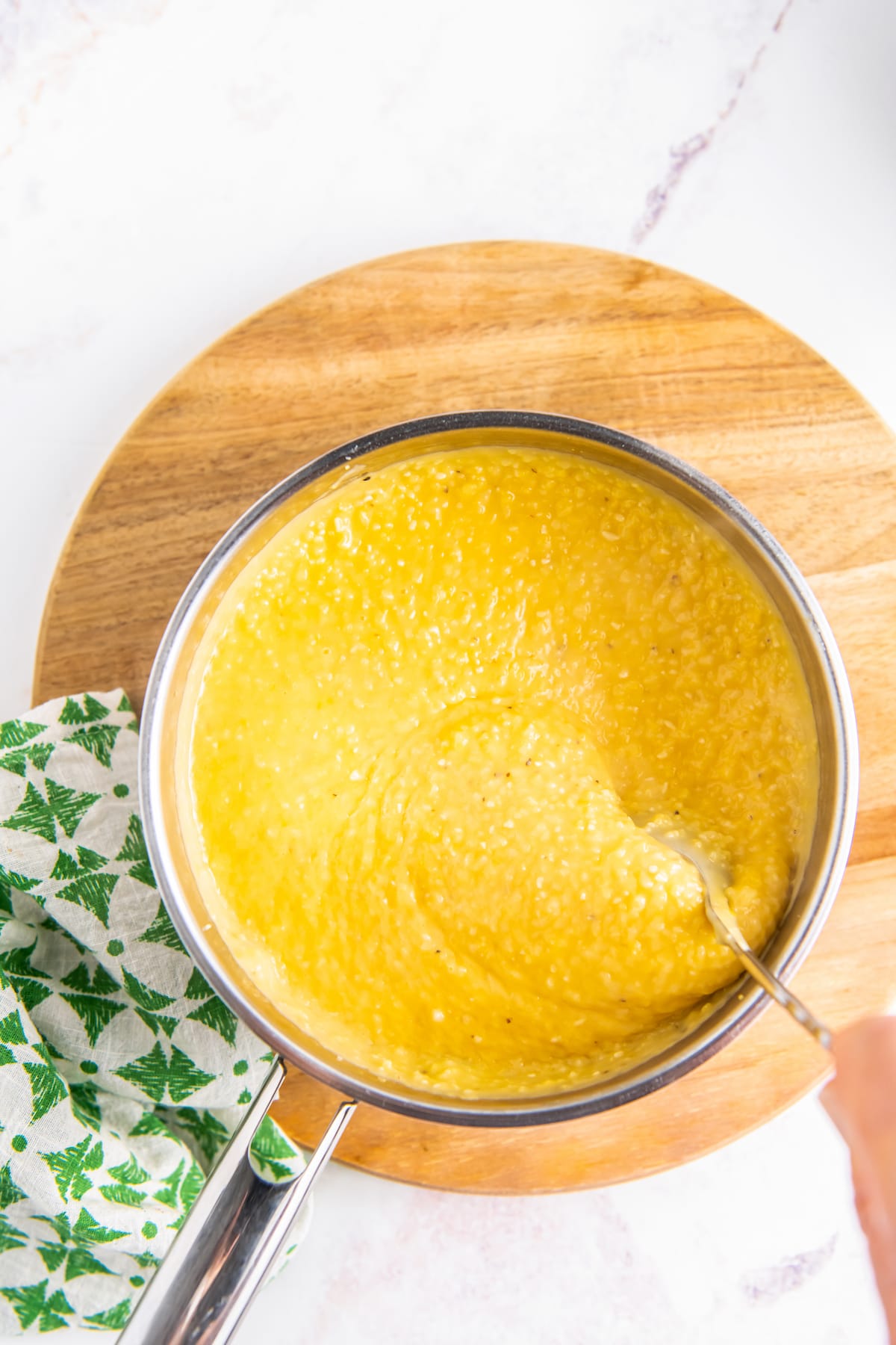 a pan of yellow grits on top of a round cutting board with a green napkin next to it