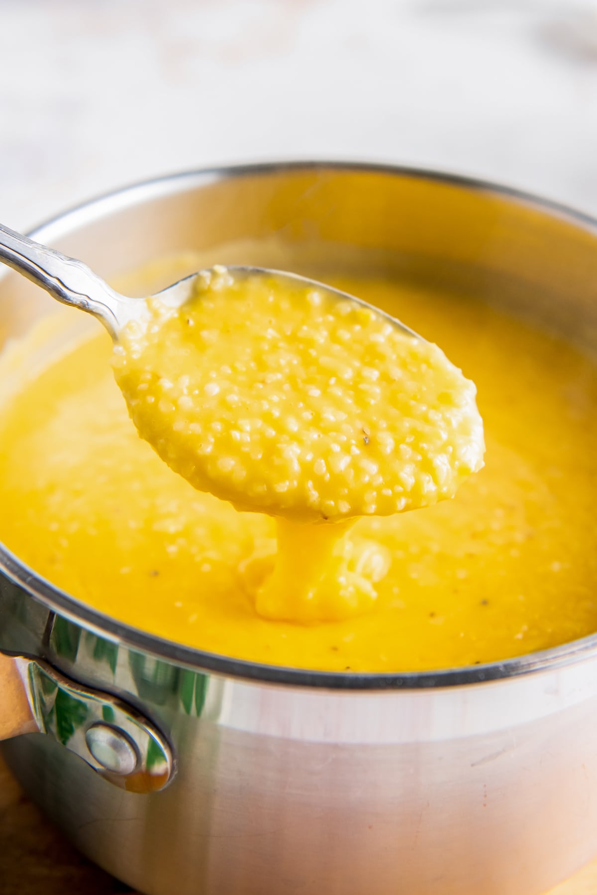 a saucepan with yellow grits being stirred with a spoon