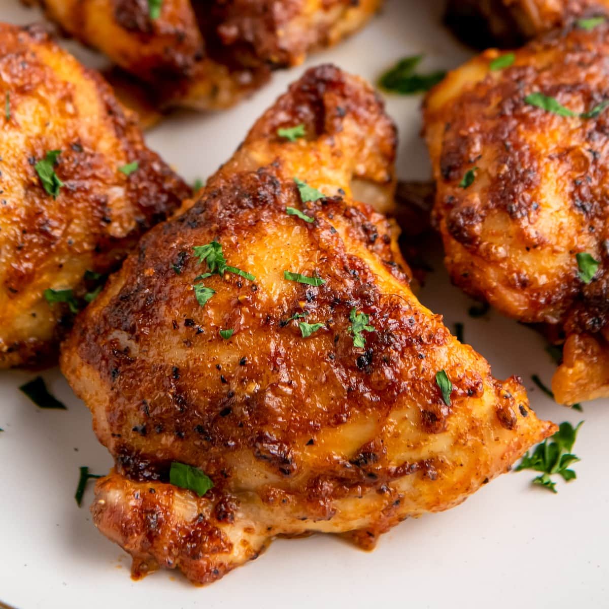 Air fryer chicken thighs on a plate with fresh herbs sprinkled on top.