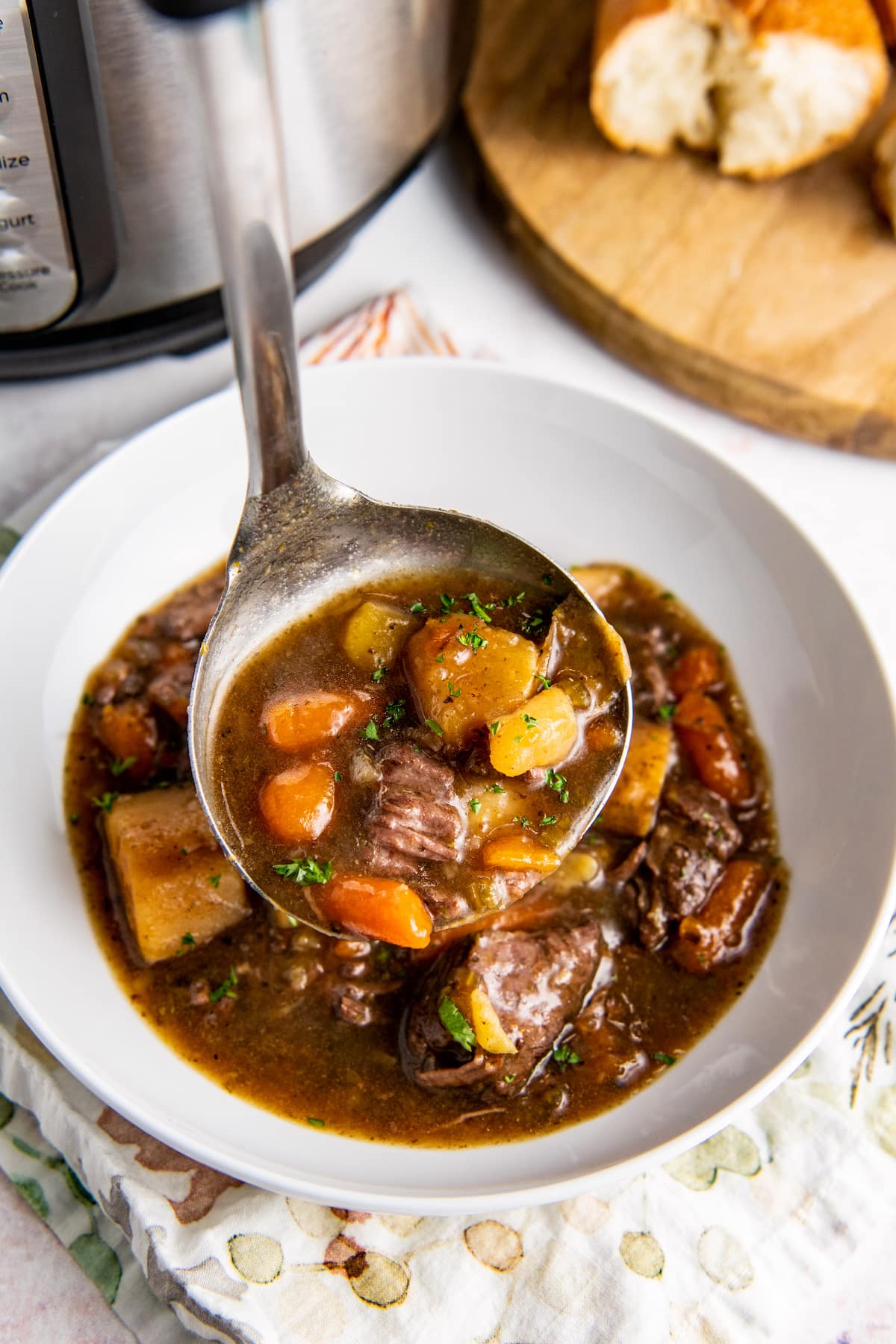 A ladle shows a close-up of beef stew with carrot and potatoes with