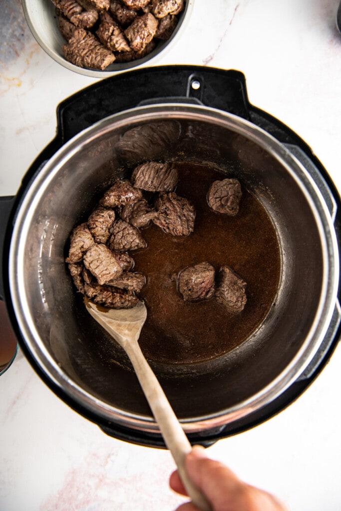 Beef is shown with a wooden spoon in an instant pot.