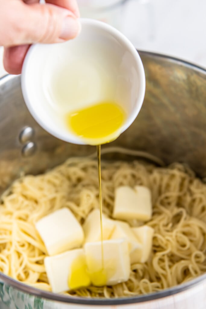Olive oil is added to a pot with noodles and butter.