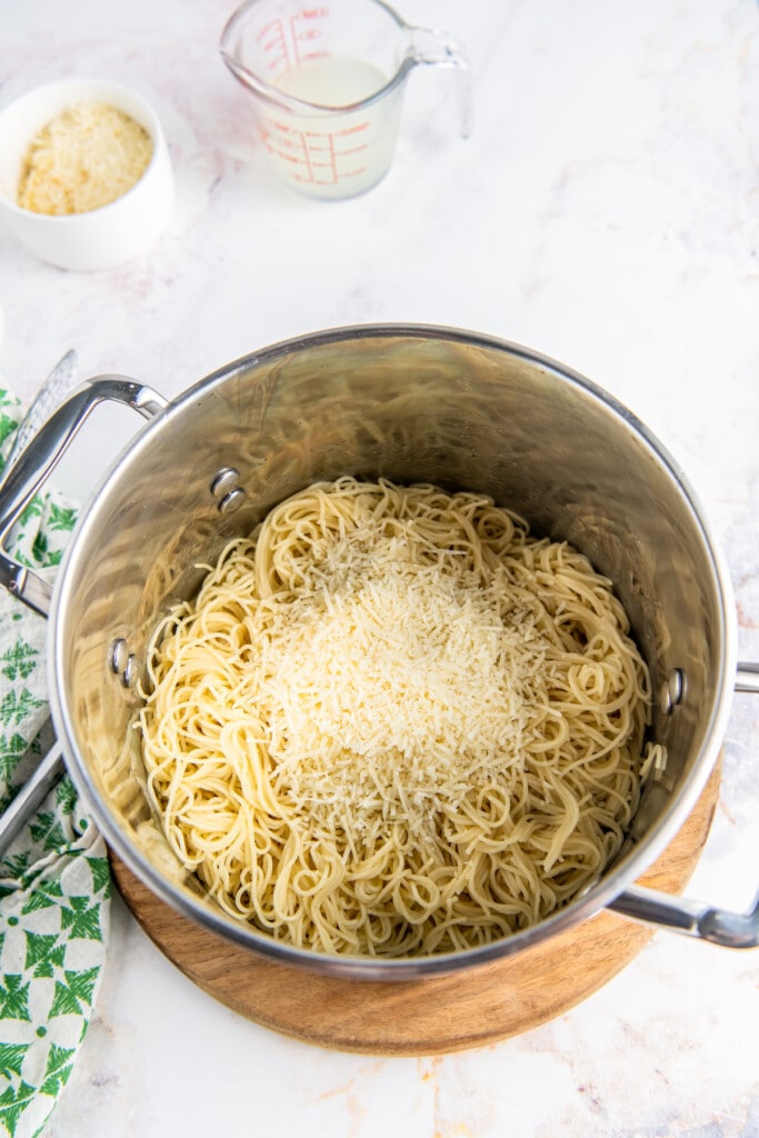 Parmesan cheese is added to a pot of cooked noodles.