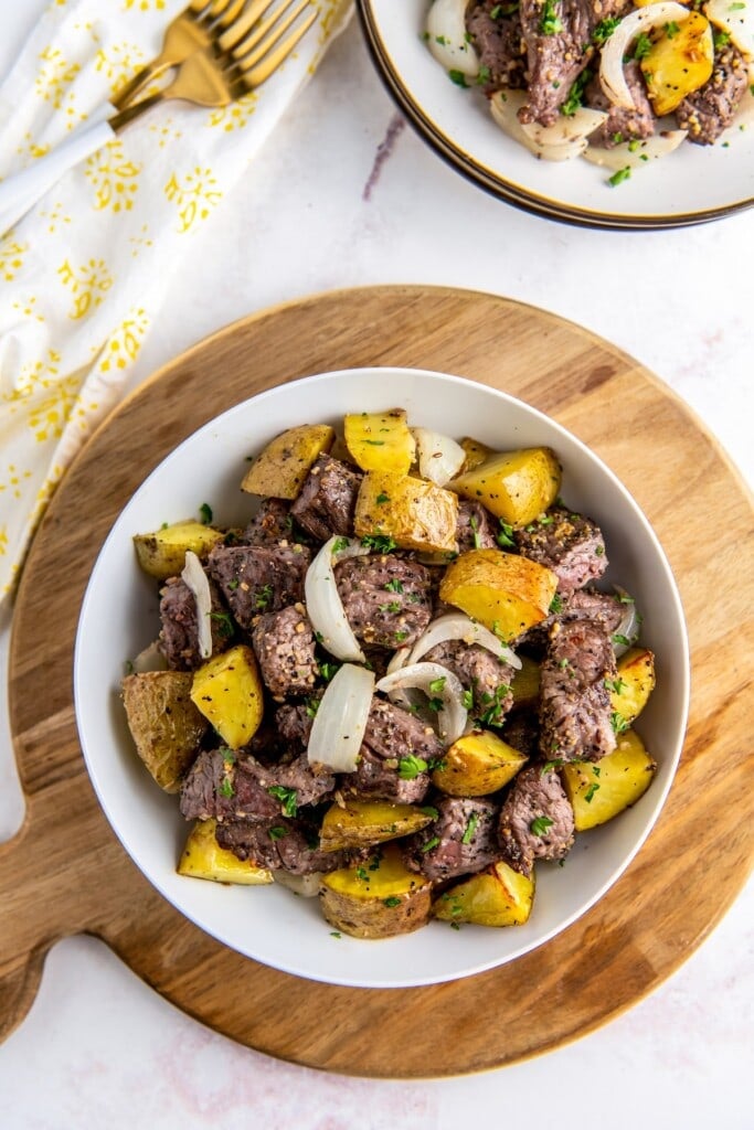 Plate of steak bites with onion slices and potatoes.