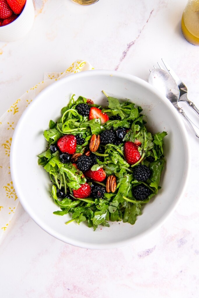 Arugula and chopped berries in a mixing bowl.