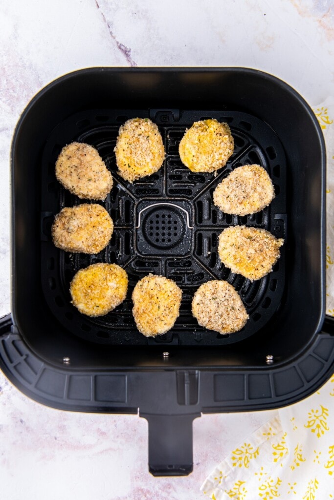 Breaded slices of goat cheese in the basket of an air fryer.