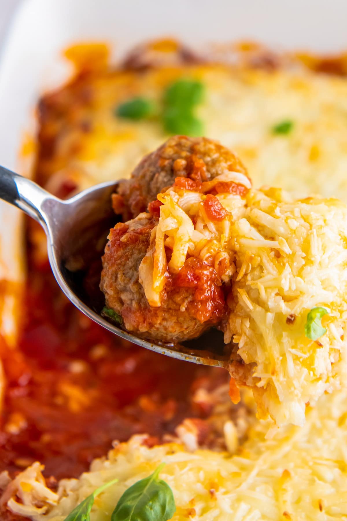 Meatballs smothered in tomato sauce and cheese on a spoon.