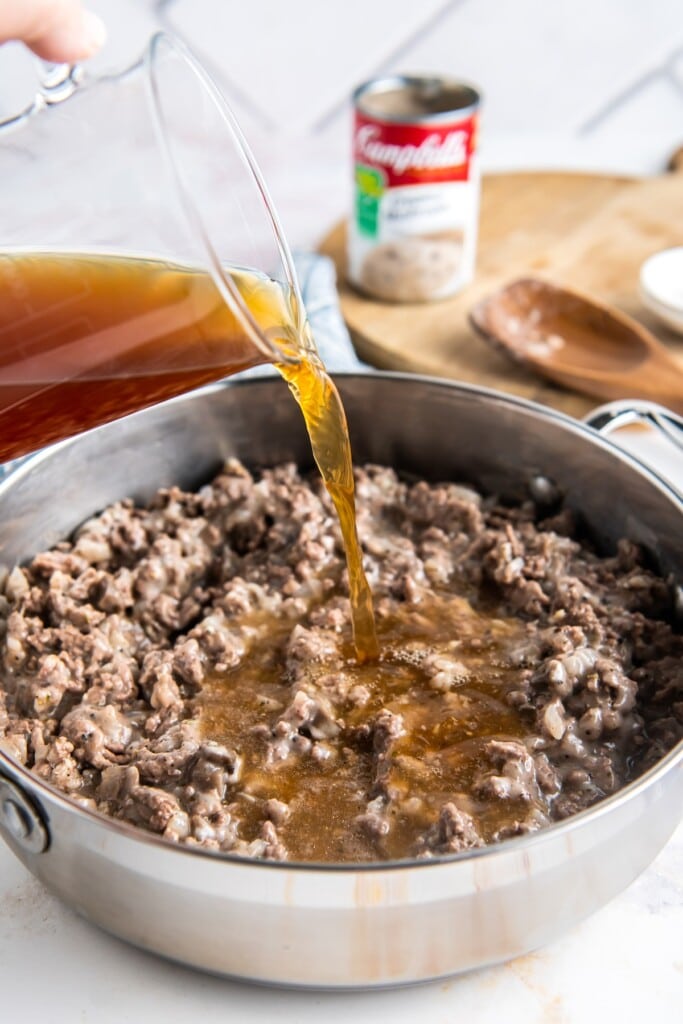 Broth being poured over browned ground beef.