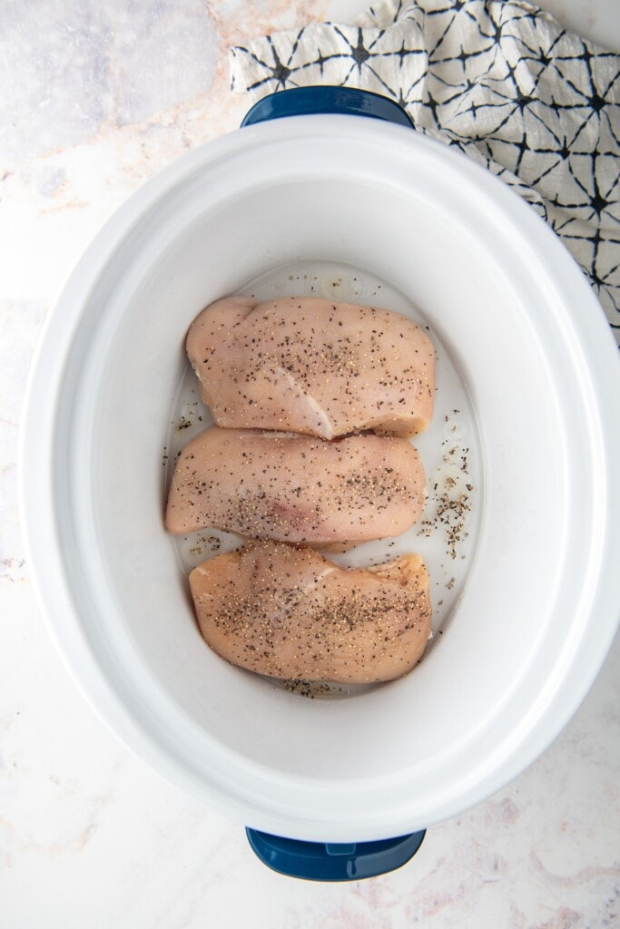 Chicken breast in a crockpot seasoned with salt and pepper.