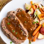 Meatloaf covered in sauce on a plate with veggies.