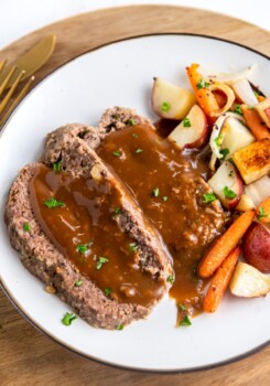 Meatloaf covered in sauce on a plate with veggies.