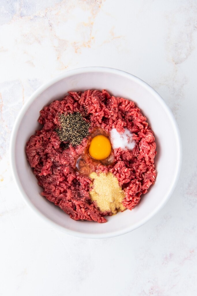 Ground beef in a bowl with seasoning and a cracked egg.