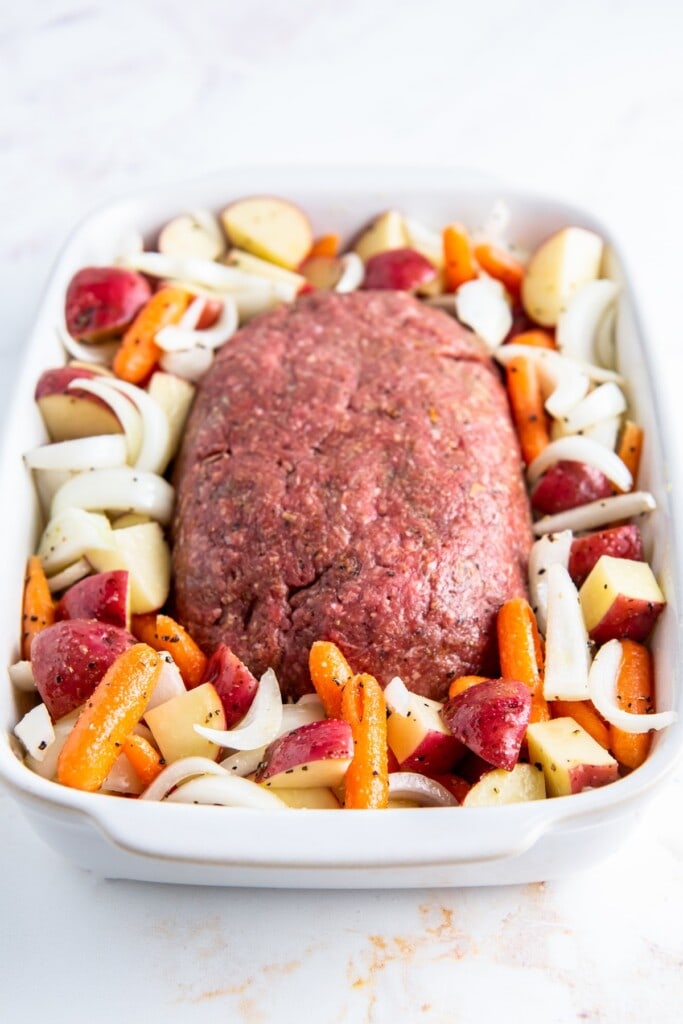 A loaf of ground beef surrounded by chopped vegetables.