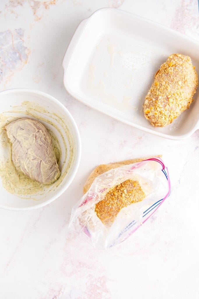 Chicken breasts being coated in mayo and cracker crumbs, and then placed in a baking dish.