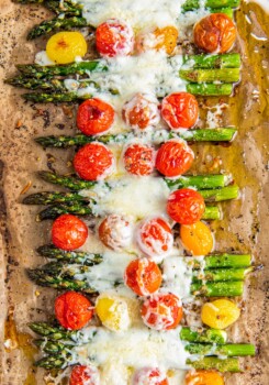 Roasted asparagus and tomatoes covered in cheese.