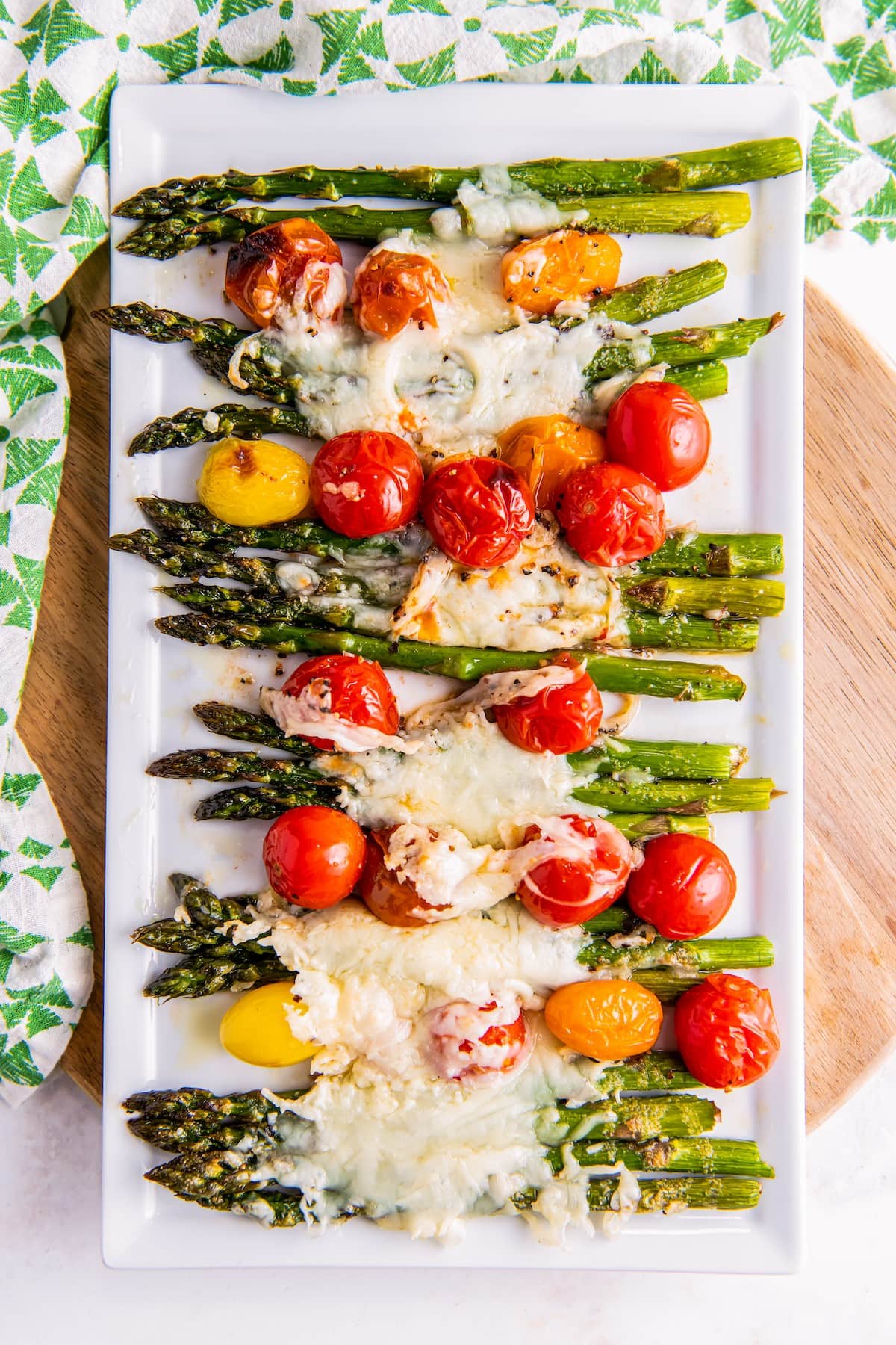 Roasted asparagus and cherry tomatoes on a plate, covered in cheese.