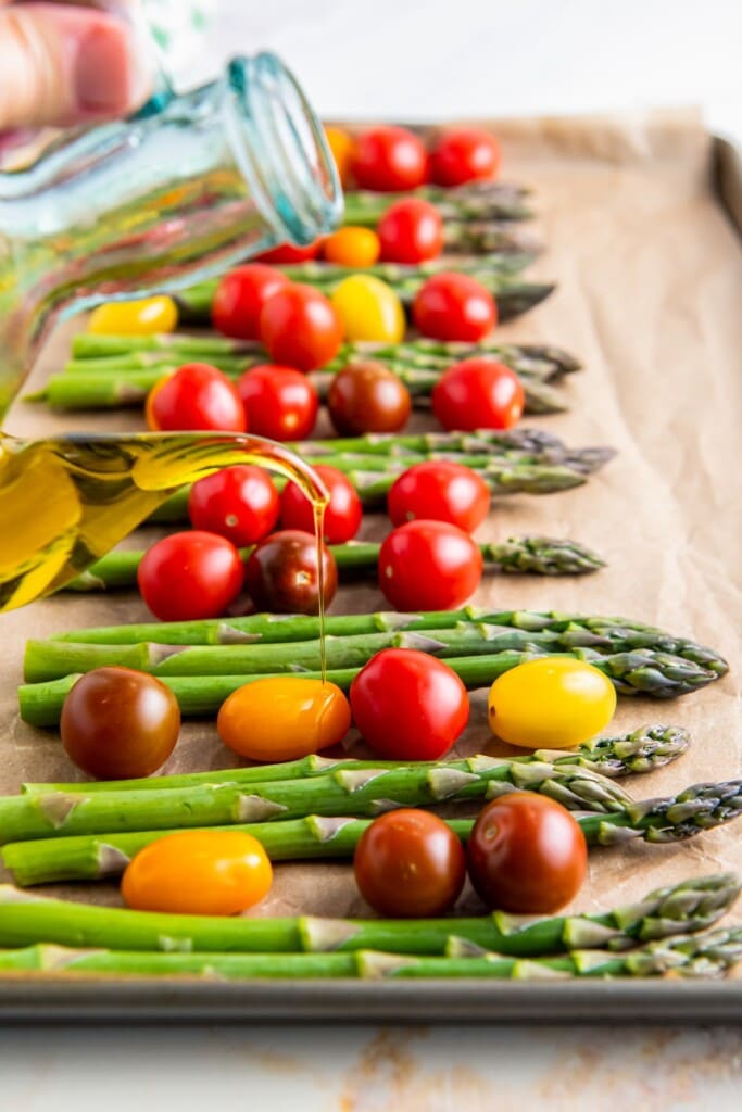 Olive oil poured over a tray of cherry tomatoes with asparagus.