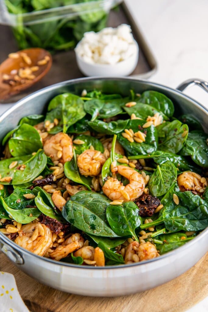 Orzo and shrimp mixed with fresh spinach in a pan.