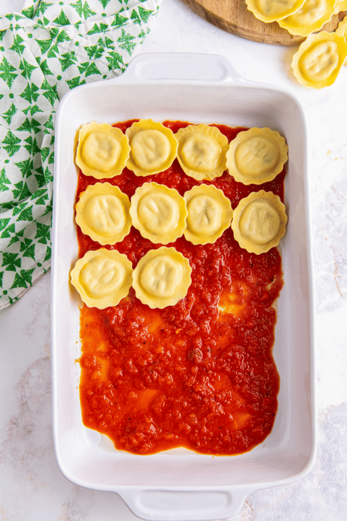 Baking dish covered with sauce and layered with fresh ravioli.