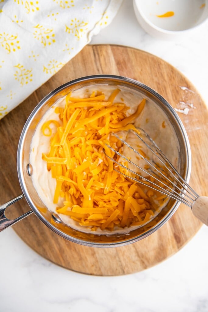 Shredded cheddar cheese added to a sauce pan.