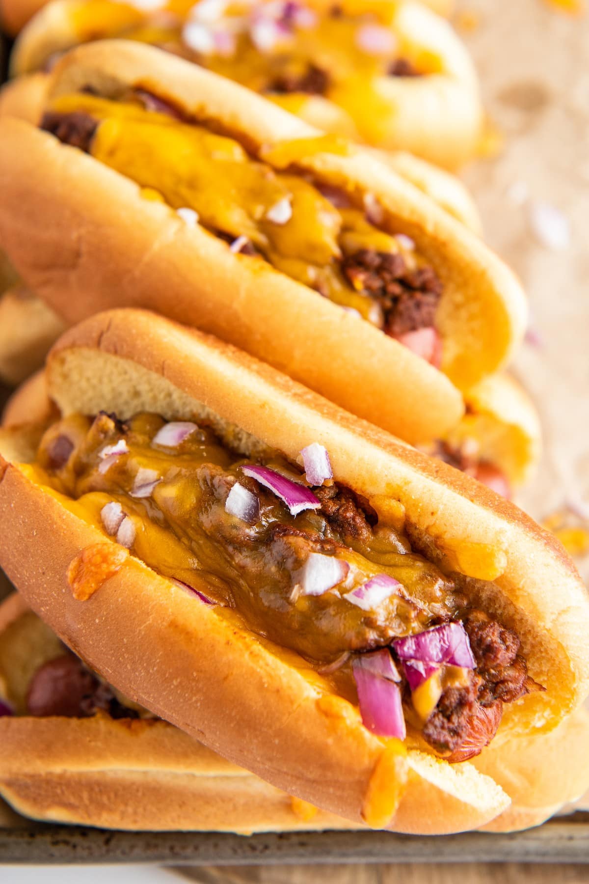 Chili cheese dogs sprinkled with chopped red onion.