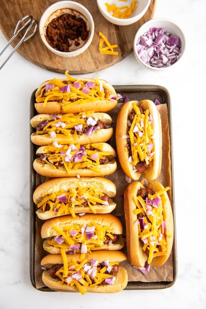 Chili dogs topped with shredded cheddar cheese and chopped onion.